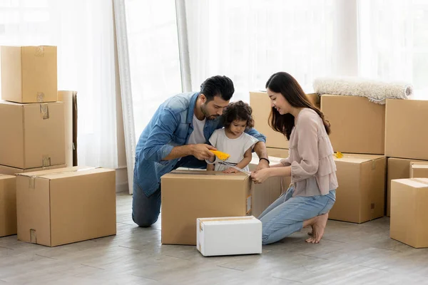 The family just bought new furniture and helped organize the house. Mon dad and daughter just moving new home. They unpacking parcel box and arranging on the floor in the living room.