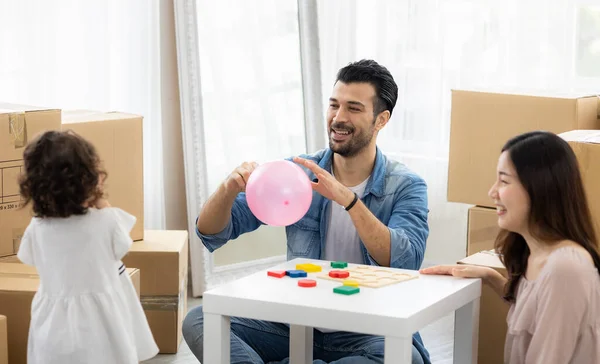 Parents and daughters play with pink balloon sitting on the floor in the living room at home. The family just moved to a new house. Happy moment Multi-ethnic dad mom and child.