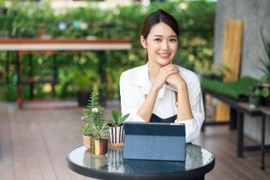 Ev bitkilerinde çalışan Asyalı genç ve tatlı bir kadın. Asyalı kadın bahçıvan, seradaki ağaçların büyümesini kaydetmek ve yakalamak için tablet kullanıyor. Ev konseptinden küçük işletme çalışmaları başlat.