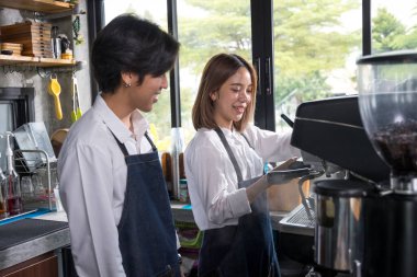 İki Asyalı garson kahve dükkanında bir fincan sıcak kahve yapıyor. Kahveci dükkanda kahve makinesiyle çalışıyor. Barista kahve makinesini kullanmayı öğretiyor..