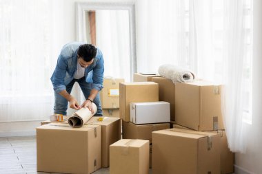 Genç adam yeni bir eve taşınıyor. Paketleri açıyor ve oturma odasının zeminini düzenliyor..
