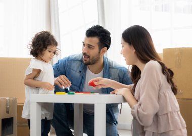 Ebeveynler ve kızları evdeki oturma odasında yerde oturan tahta bloklarla oynuyorlar. Aile yeni bir eve taşındı. Mutlu an. Çok ırklı baba, anne ve çocuk..