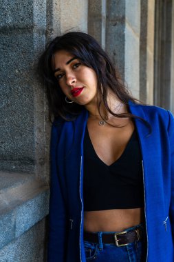 Gri duvara yaslanan genç bir kadın. Kot pantolon ve mavi bir Amerikan ceketi giyiyor. Fotoğraf La Laguna, Tenerife 'de çekildi..