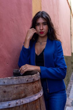 Young woman leaning on a wine barrel used as a table in a restaurant. She wears jeans and an American jacket. The photo was taken in La Laguna, Tenerife.