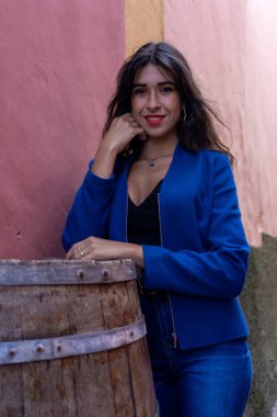 Young woman leaning on a wine barrel used as a table in a restaurant. She wears jeans and an American jacket. The photo was taken in La Laguna, Tenerife.