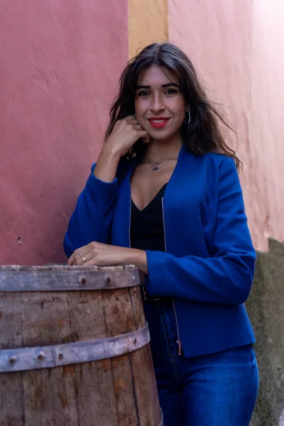 Young woman leaning on a wine barrel used as a table in a restaurant. She wears jeans and an American jacket. The photo was taken in La Laguna, Tenerife.