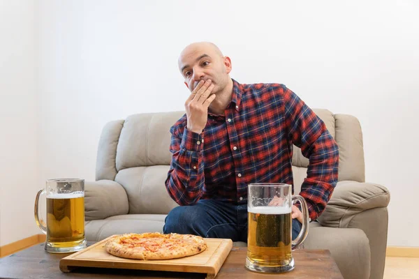 Guy waiting for friend with italian pizza and a mug full of beer at home