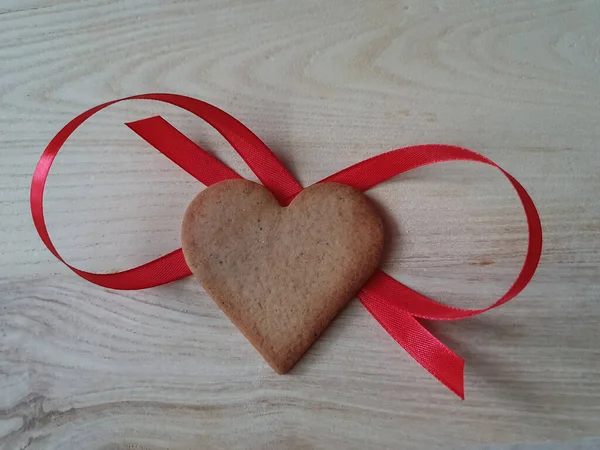 Pain d'épice maison en forme de coeur décoré avec un ruban rouge sur un fond en bois clair, Saint Valentin, carte de souhaits, pâtisserie, Copier l'espace, vue sur le dessus, concept d'amour, fiançailles, amour — Photo