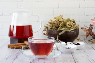 Beyaz duvarın önündeki tahta bir çaydanlıkta demlenmiş çeşitli otlar. Linden, nar çiçeği, yeşil çay, üzüm tohumu, zeytin yaprağı, tarçın çubukları ve cam bir fincanda kurumuş gül..