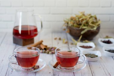 Beyaz duvarın önündeki tahta bir çaydanlıkta demlenmiş çeşitli otlar. İki bardak ıhlamur, nar, yeşil çay, üzüm tohumu, zeytin yaprağı, tarçın çubuğu ve kurutulmuş gül..