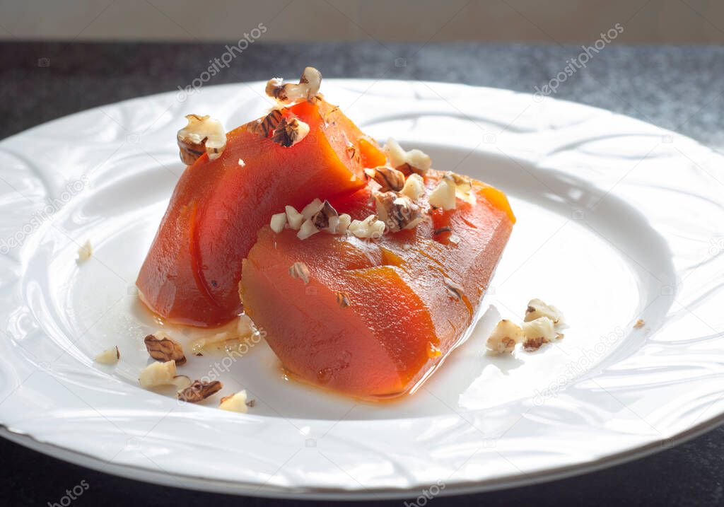 Pumpkin dessert with walnut sprinkles cooked with steamed sugar, on a white plate.