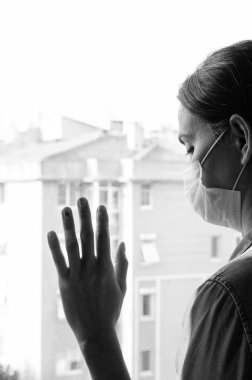 Koronavirüs salgını sırasında evde sosyal mesafe için maske takan üzgün bir kadın. Kaygı, stres, zihinsel, sağlık, kriz