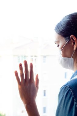 Koronavirüs salgını sırasında evde sosyal mesafe için maske takan üzgün bir kadın. Kaygı, stres, zihinsel, sağlık, kriz