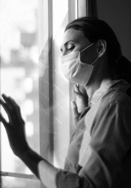 Koronavirüs salgını sırasında evde sosyal mesafe için maske takan üzgün bir kadın. Kaygı, stres, zihinsel, sağlık, kriz