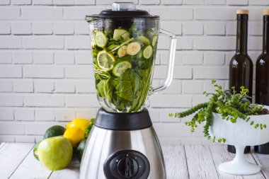 Mutfak blendırında yeşil meyve püresi hazırlama süreci. Sağlıklı yemek için yeşil smoothie. Beyaz duvarın önünde.