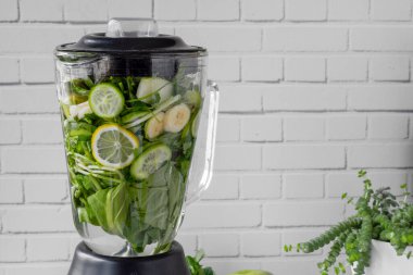 Mutfak blendırında yeşil meyve püresi hazırlama süreci. Sağlıklı yemek için yeşil smoothie. Beyaz duvarın önünde.