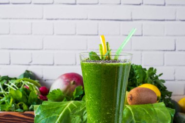 Duvarın önünde yeşil meyve ve sebzelerle harmanlanmış sağlıklı bir içecek, üzerine chia tohumları serpiştirilerek servis edilir. içeriklerle