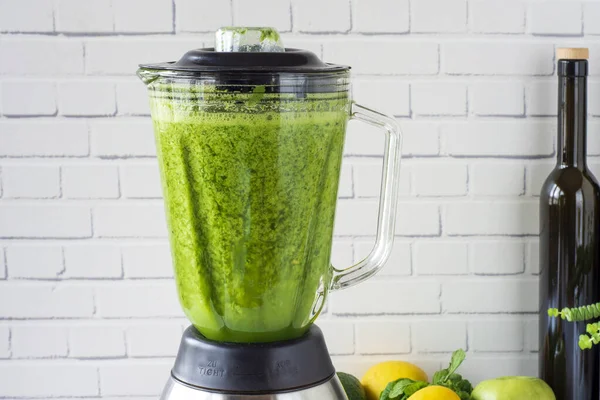 Duvarın önünde yeşil meyve ve sebzeler ve harmanlanmış sağlıklı bir içecek hazırlandı. Mutfak blendırında yeşil smoothiein hazırlama işlemi, sıvılaştırıcı.