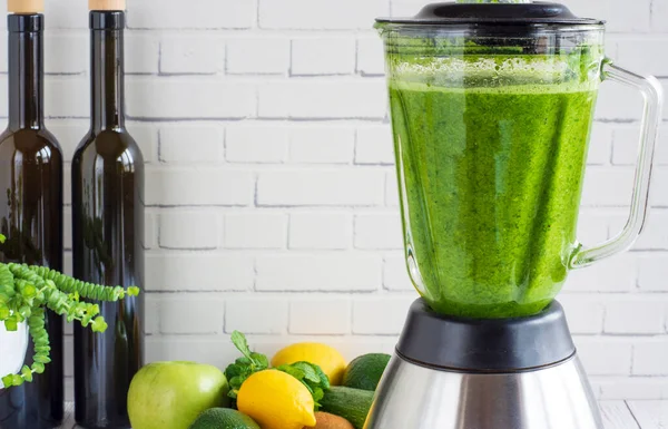 Duvarın önünde yeşil meyve ve sebzeler ve harmanlanmış sağlıklı bir içecek hazırlandı. Mutfak blendırında yeşil smoothiein hazırlama işlemi, sıvılaştırıcı.