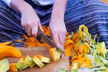 Tatlı kabaklı börek yapıyorum. Bir kadın evdeki mutfakta yerde otururken balkabağını kesiyor ve kesiyor..