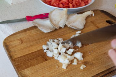 Kadın taze istiridye mantarlarını ince ince doğruyor. İstiridye mantarlı sahte kokore, Pleurotus ostreatus. Chili biberi, kekik, biber, domates,