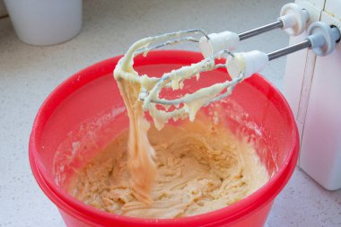 Kurabiye hamuru kırmızı kaseye karıştırılıyor. Yetişkin kadın salgında lezzetli ve çıtır çıtır kurabiyeler pişiriyor.