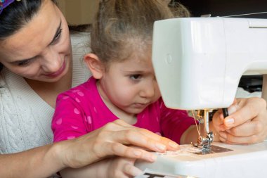 little girl is learning from her mother to use a sewing machine. selective Focus girl
