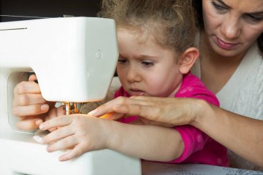 little girl is learning from her mother to use a sewing machine. selective Focus girl