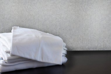 Beton duvarın önünde ve siyah zeminde beyaz giysi yığını. Gömlek ve tişörtler