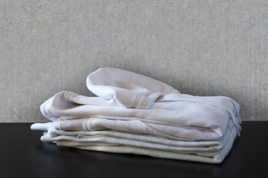 Beton duvarın önünde ve siyah zeminde beyaz giysi yığını. Gömlek, tişört ve kazak. 