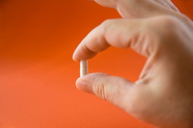 El ve parmaklar turuncu arka planda ilaç kapsülünü tutuyor. Seçici odak hapı..