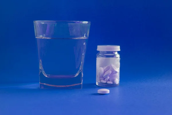 a glass of water, bottle and medicines, pills, drugs. isolated. Blue Background.