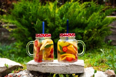 İki kavanoz cam, kırmızı, turuncu ve sarı meyveli lezzetli detoks içeceği, taşın üzerinde duruyor. Seçici Odak Gözlükleri.