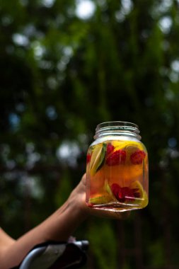 Kavanozda kırmızı turuncu ve sarı meyvelerden oluşan enfes bir detoks içeceği tutan kadın. Seçici Odaklanma İçeceği.