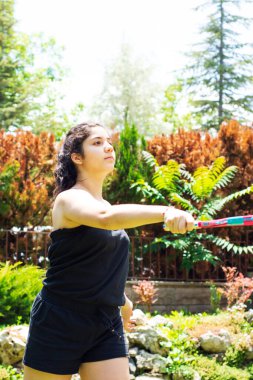 Genç kız bahçede tenis raketi ve topla oynuyor.