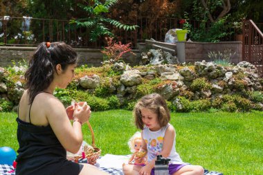 Küçük kız ve kız kardeşi oyun oynuyorlar ve bahçede piknik yapıyorlar.