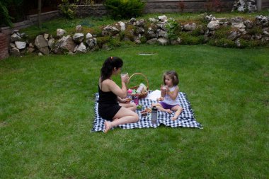 Küçük kız ve kız kardeşi oyun oynuyorlar ve bahçede piknik yapıyorlar.