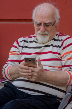 Yaşlı adam evinin önünde oturuyor, cep telefonuyla uğraşıyor. Zar zor görebiliyorum.