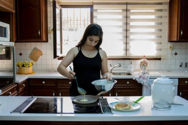 Genç kız, evinin mutfağında kahvaltı için krep pişiriyor. Seçici Odaklanma Kızı