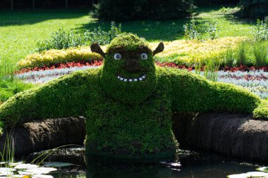 Ukrayna, Kiev, 01.08.2025. Dev figürü, çizgi film karakteri Shrek. Şehir parkında ya da bahçede yeşil yapraklı bir çalılığın dalları olan bir tasarım. Shrek karakteri Bataklık Hamamında oturuyor. Yazı