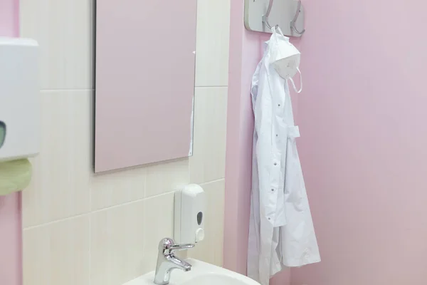 Doctors office in a real hospital. White robe and mask on a hanger. Selective focus.