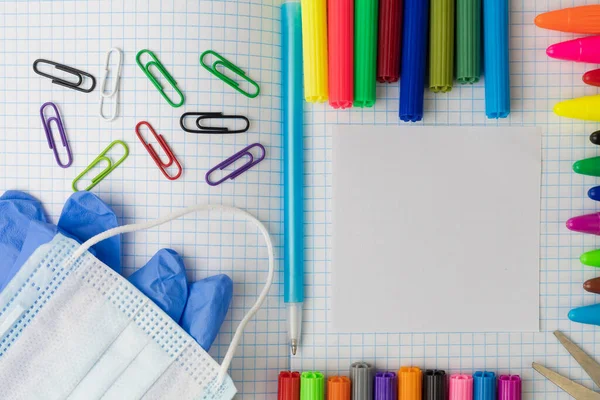 Kare bir egzersiz kitabındaki okul malzemeleri. Yazı veya metin için fotokopi alanı var. Maske ve tıbbi eldiven. Renkli kalemler ve dağınık ataçlar..
