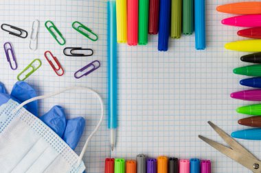 Kare bir egzersiz kitabındaki okul malzemeleri. Yazı veya metin için fotokopi alanı var. Maske ve tıbbi eldiven. Renkli kalemler ve dağınık ataçlar..