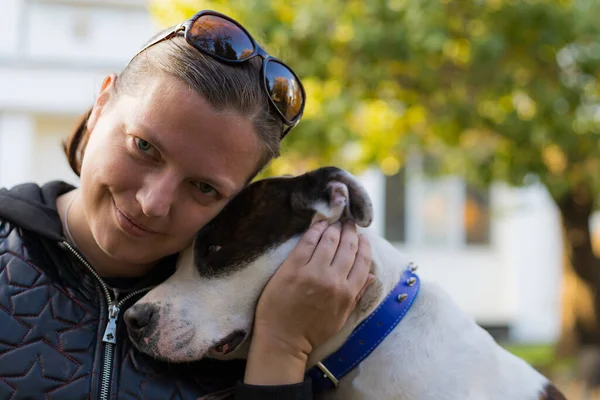 Genç bir kadın, sevgili evcil hayvanı pitbull 'la şehir parkında arkadaşlık etmekten zevk alıyor. Bulanık arkaplanı olan seçici odaklanma. Sığ alan derinliği.