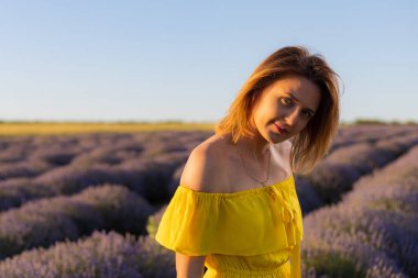 Sarı elbiseli güzel ve güzel genç bir kadın gün batımında lavanta tarlasında yürümekten hoşlanıyor.