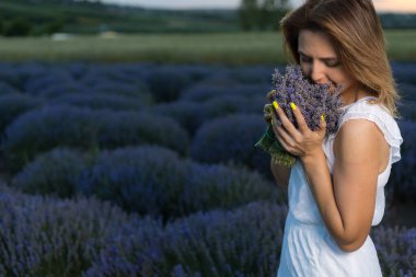 Beyaz elbiseli güzel ve güzel genç bir kadın gün batımında lavanta tarlasında yürüyüş yapmaktan hoşlanıyor. Bulanık arkaplan ile seçmeli odak.
