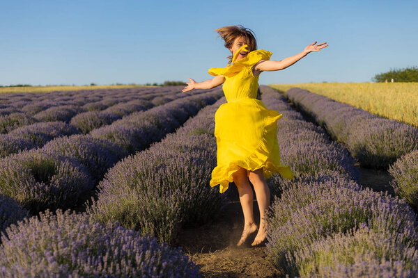 Красивая и красивая молодая женщина в желтом платье расслабляется и наслаждается прогулкой по лавандовому полю на закате, тонизируется