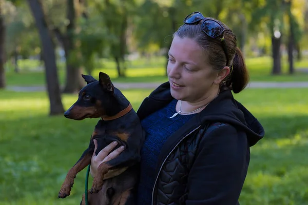 都会の公園で大好きなピンチャー犬と一緒に楽しむ若い女性 背景がぼやけた選択的フォーカス フィールドの浅い深さ — ストック写真