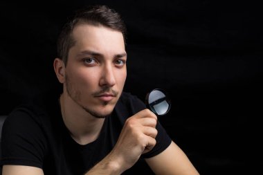 Genç yakışıklı bir adam ve siyah arka planda gösterişsiz bir büyüteç. Arama sembolü. Soruşturma kavramı