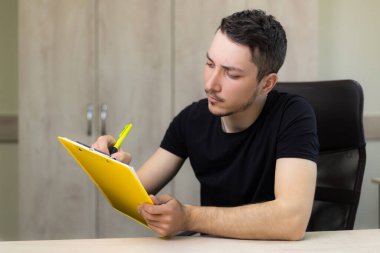 Genç, yakışıklı bir adam ya da yetişkin bir adam ofisin bulanık bir arka planı üzerinde çalışıyor..